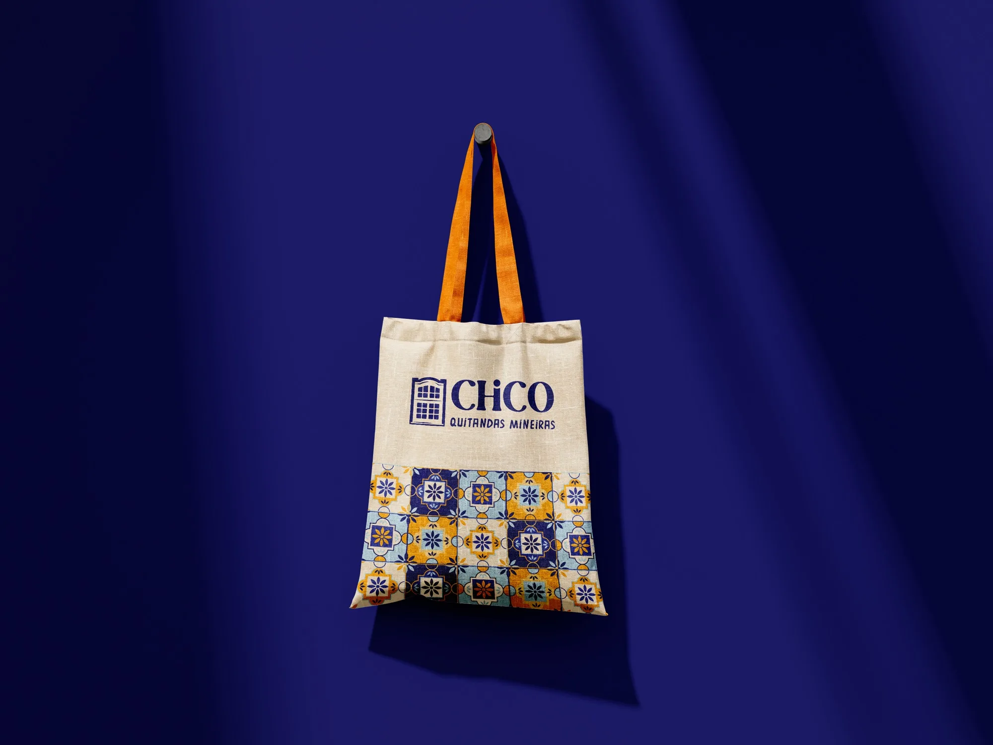 Sacola ecobag da Chico Quitandas Mineiras pendurada, com logotipo e estampa de azulejos