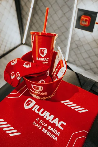 Copo, meias e balde vermelhos com o logotipo ILUMAC, apoiados sobre a sacola de algodão da marca