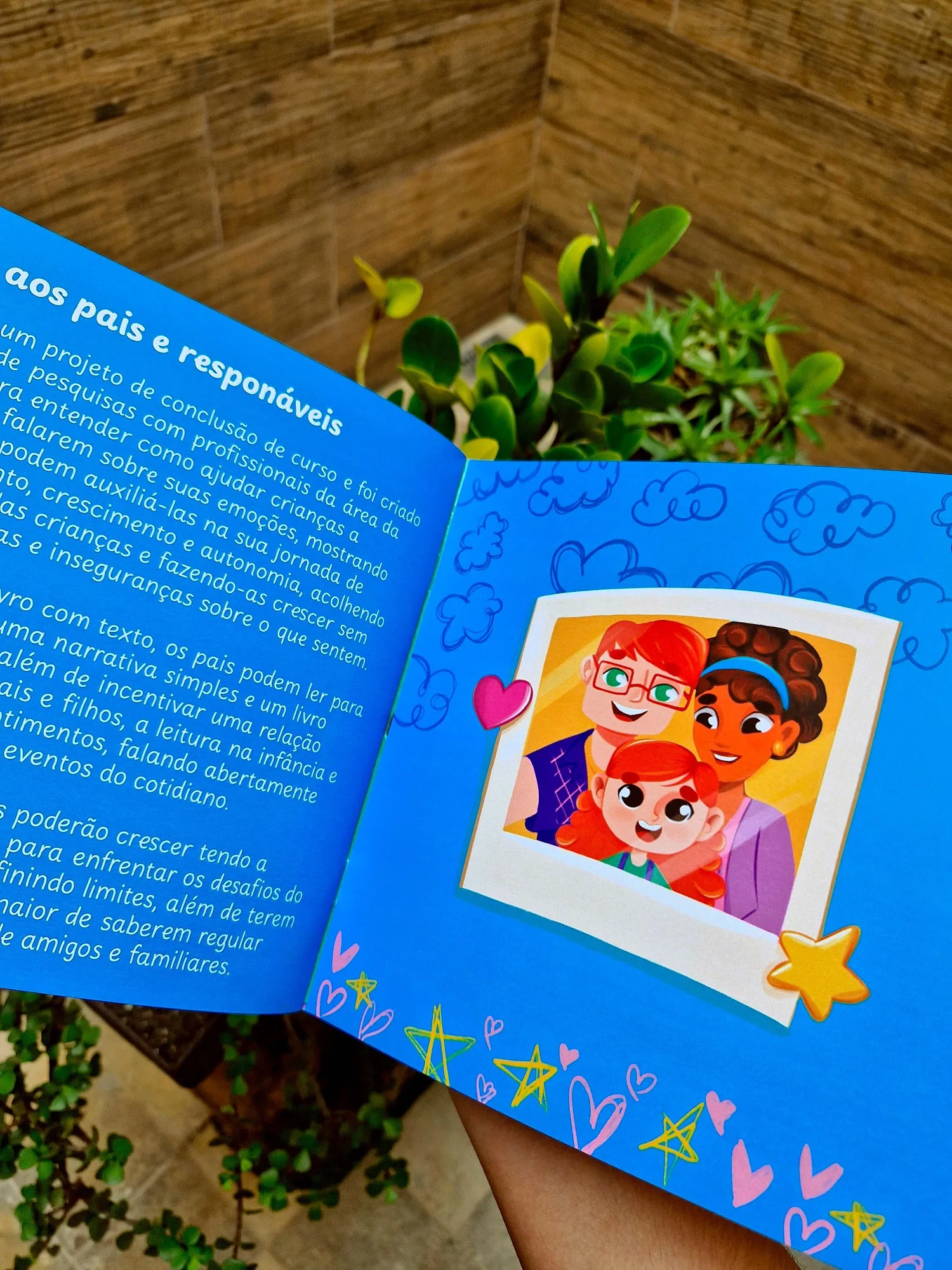 Página dupla 'Aos pais e responsáveis' do livro impresso, ao lado de uma foto polaroid ilustrada de família